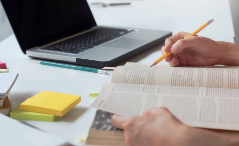 persona che studia su un libro con un computer portatile accanto