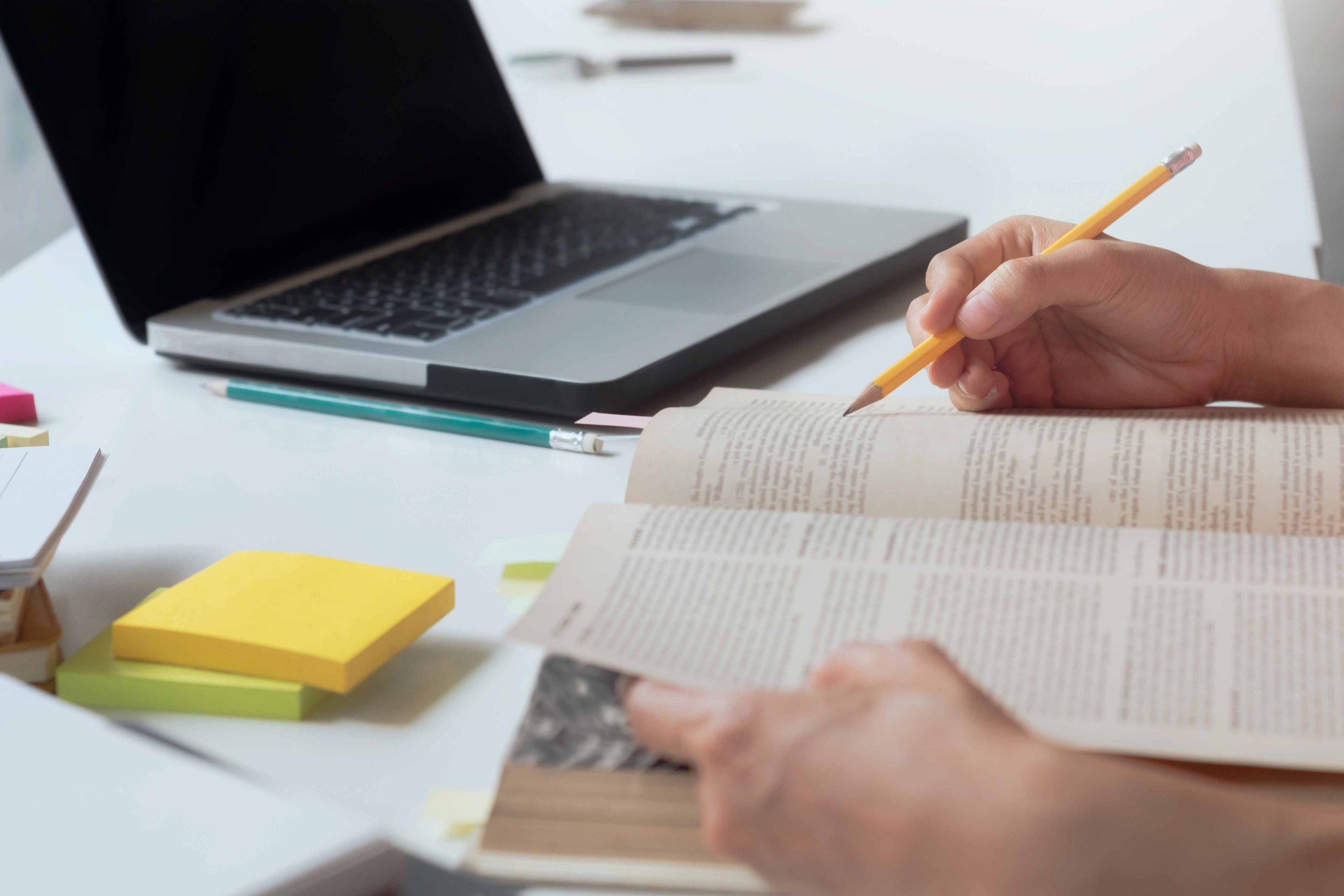 persona che studia su un libro con un computer portatile accanto